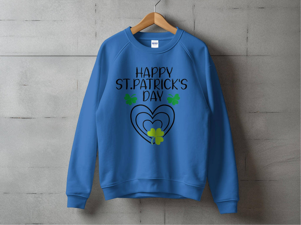 A festive blue Garment Graphics sweatshirt on a wooden hanger against a concrete wall displays Happy St. Patricks Day in black, surrounded by three green shamrocks and a heart design beneath the cheerful clover motif.