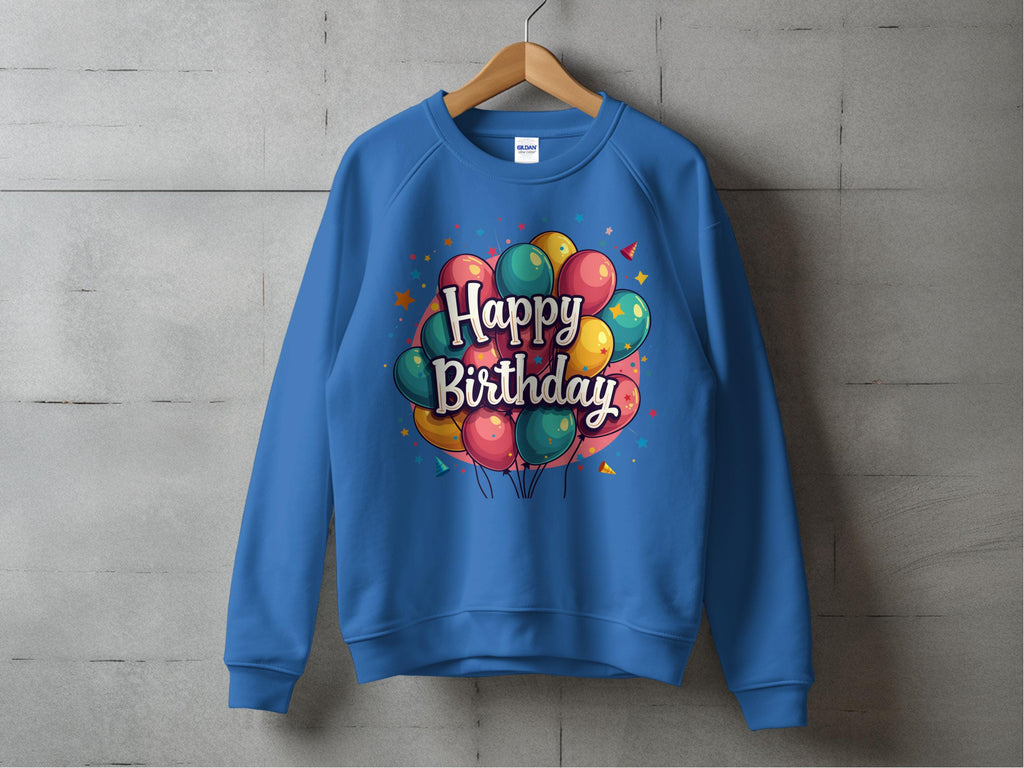 A Garment Graphics blue sweatshirt with colorful Happy Birthday balloons and bold letters is displayed on a wooden hanger against a gray concrete wall. Its unisex sizing makes it perfect for anyone ready to celebrate in comfort and style.
