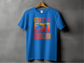 A Garment Graphics blue Born to be a Musician T-shirt, featuring bold text and silhouettes of a drummer and guitarist against a vibrant sunset design, hangs on a wooden hanger against a gray background—ideal for music lovers.