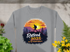 Garment Graphics offers a gray unisex sweatshirt featuring a hiker silhouette against mountains and a sunset with Retired 2025, Not My Problem Anymore. The design, surrounded by plants and flowers on concrete, caters to outdoor lovers.