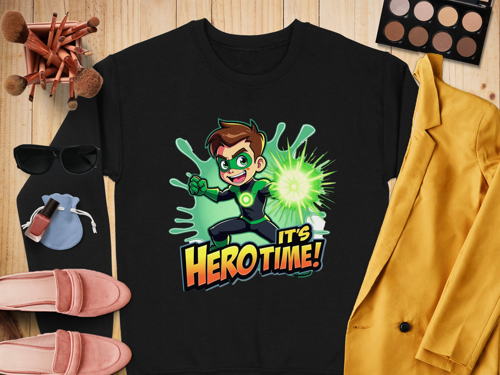 The Garment Graphics black unisex t-shirt features a cartoon character with green goggles and gloves holding a glowing green object, with the phrase Its Hero Time! Its artfully staged alongside yellow jacket, eyeshadow palette, makeup brushes, sunglasses, purse, and shoes.