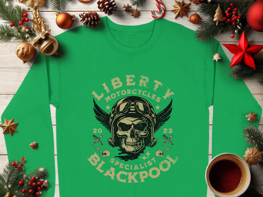 Garment Graphics offers a green shirt featuring a Liberty Motorcycles Specialist Blackpool design with a skull adorned with goggles and wings, surrounded by pine branches, ornaments, a wrapped gift, an orange, and a drink on wood.