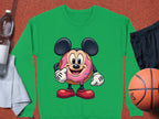Garment Graphics fun staple, this green sweatshirt features a quirky cartoon character with big ears and red shoes, enjoying a donut. Styled on terracotta with essentials including a white towel, water bottle, black shorts, and basketball.