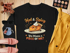 A Garment Graphics black pie graphic sweatshirt featuring a cartoon pie slice and the phrases Hot & Spicy and You Wanna a Piece of Me? is styled with sunglasses, makeup brushes, a blue drawstring bag, a pink purse with matching shoes, and a yellow blazer on wooden surface.