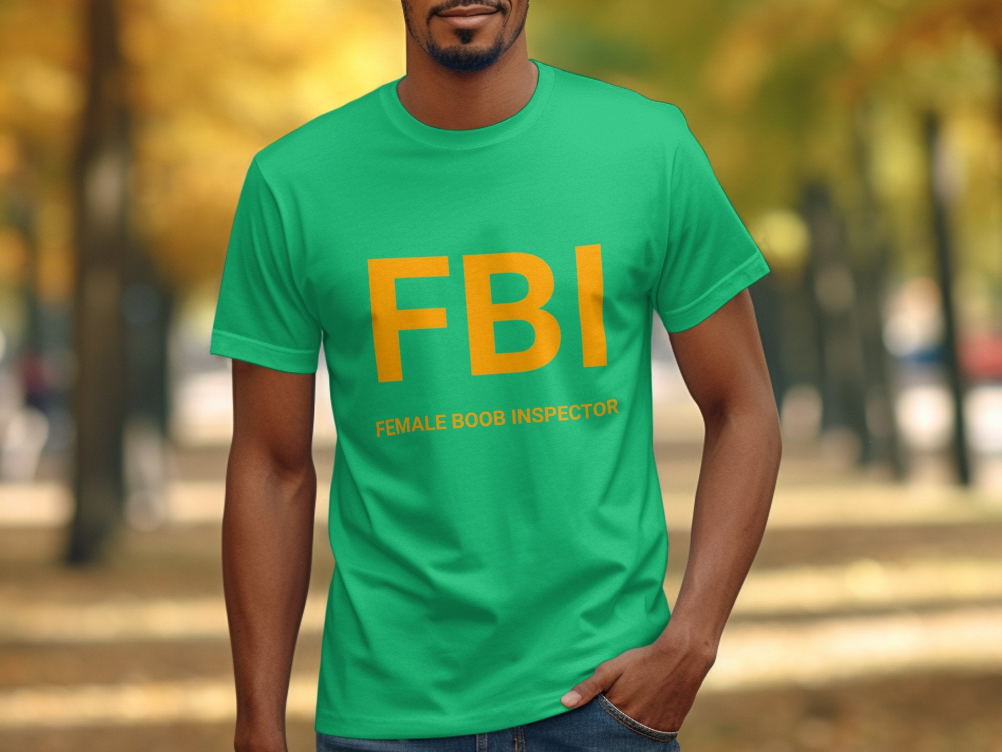 A person wears a Garment Graphics green T-shirt featuring large yellow FBI letters and humorously reveals Female Boob Inspector beneath, standing out against an autumn tree-lined path with its hilarious design.