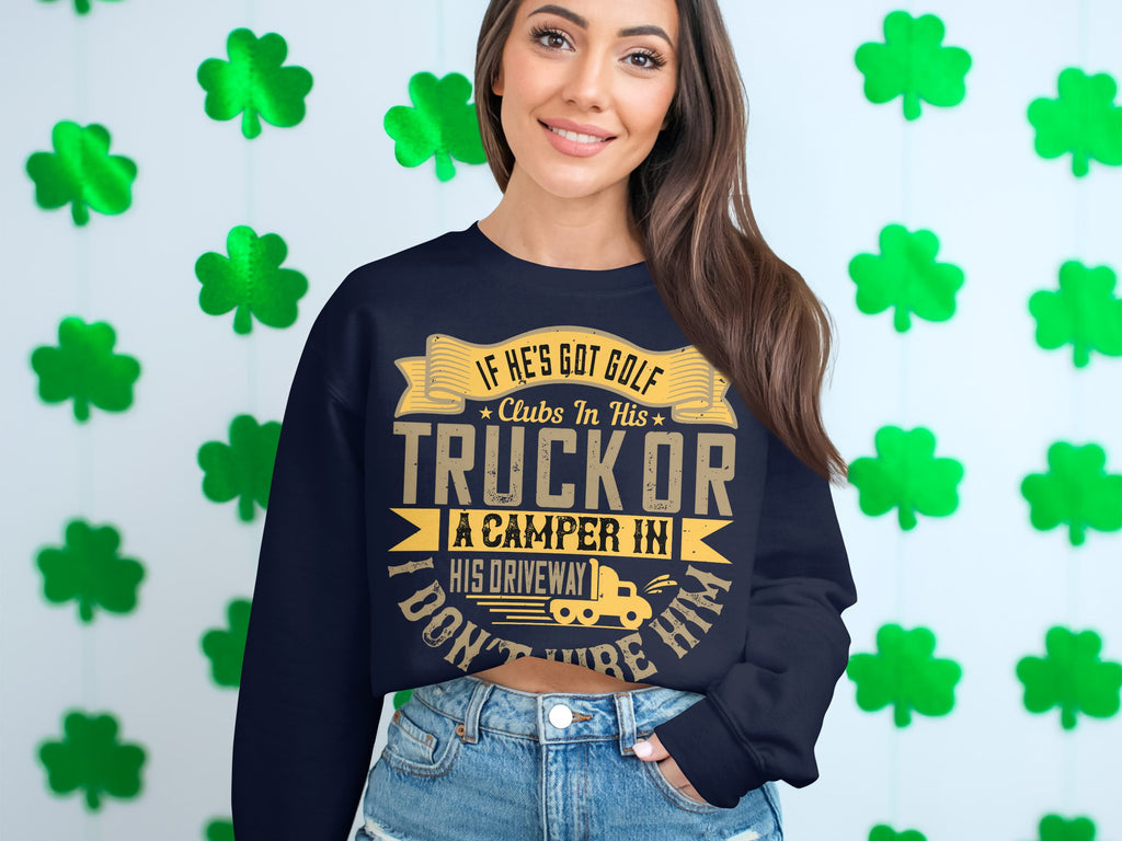 Wearing Garment Graphics humorous navy blue sweatshirt featuring the phrase, If hes got golf clubs in his truck or a camper in his driveway, I dont trust him, a person stands against a wall of green shamrocks, smiling broadly and enhancing the casual wear vibe.