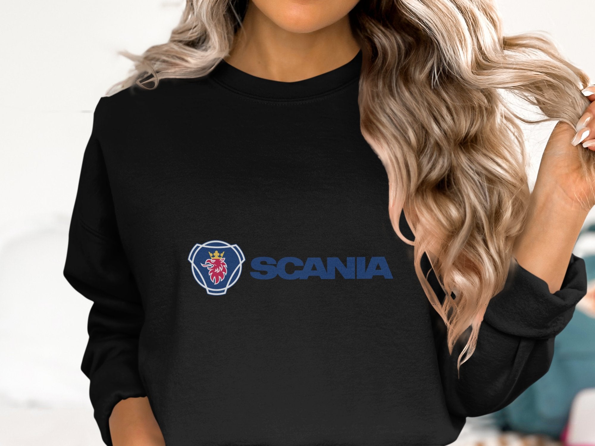 A person with long wavy hair is wearing a black Garment Graphics sweatshirt, featuring a blue text and red griffin emblem. This unisex Scania logo top is ideal for casual outings, though the persons face isnt visible.