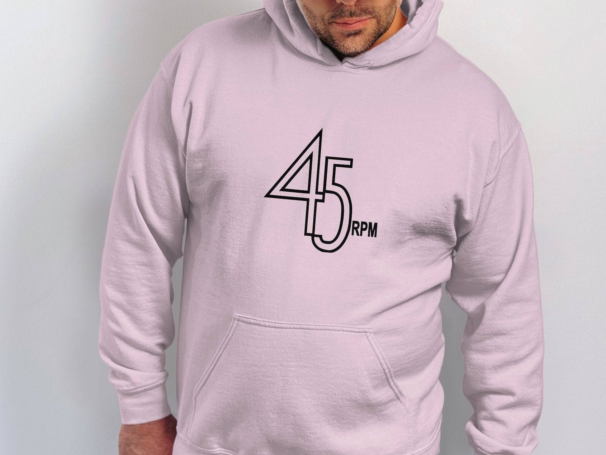 Wearing a light gray 45 RPM retro music hoodie from Garment Graphics, a person looks downward with hands at their sides, creating a striking image against the plain light-colored background. Perfect for vinyl record enthusiasts.