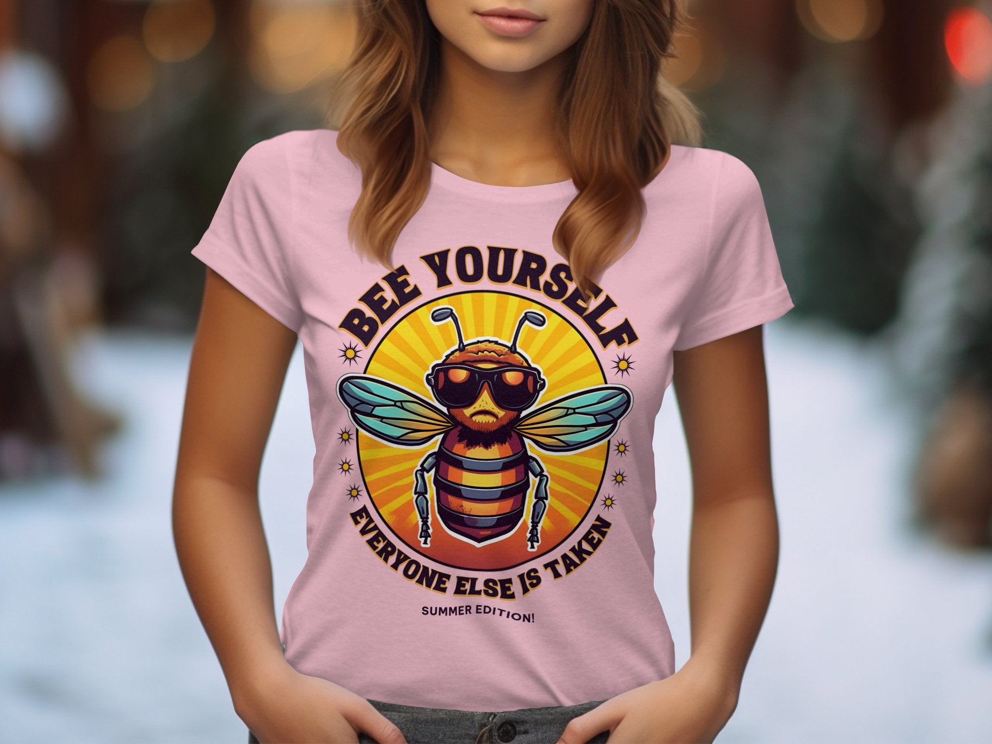A woman models a pink Garment Graphics Bee Yourself T-shirt featuring a cartoon bee in sunglasses. The shirt displays Bee Yourself, Everyone Else is Taken, Summer Edition! against a circular sunburst design and is available in womens sizes.