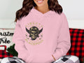 Amidst festive plaid decor, this person dons a light pink hoodie from Garment Graphics. The design features a motorcycle with a skull, wings, and the text Liberty Motorcycles Specialist, Blackpool 2023, creating an ideal style for enthusiasts.