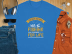 A blue Garment Graphics T-shirt with Father and Son Fishing Partners for Life in yellow and white celebrates family bonding, featuring two people fishing. Its styled with sunglasses, headphones, denim jeans, a watch, and a brown shirt on a wooden surface.