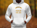 Wearing a Garment Graphics fishing hoodie featuring Father and Son Fishing For Life in gold, an individual captures the essence of fishing enthusiasts while standing amidst a blurred forest scene where autumn leaves blanket the ground.