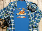 A blue T-shirt by Garment Graphics features the Hot and Spicy Pie Design with a smiling pie, whipped cream, and text Hot & Spicy, You Wanna A Piece Of Me? Styled with a checkered shirt beside a camera, headphones, and coffee cup. Perfect for family sizing fun.