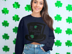 A woman exudes festive cheer in a Garment Graphics navy sweatshirt featuring a St Patricks Day leprechaun hat. Her long hair and smile shine against green shamrock patterns, perfectly paired with denim shorts.