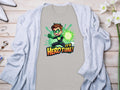 A vibrant light grey t-shirt from Garment Graphics with a Its Hero Time! superhero print lies on wood, paired with a matching cardigan, white heels, chic accessories, and delicate white flowers, setting the stage for stylish family sizing adventures.