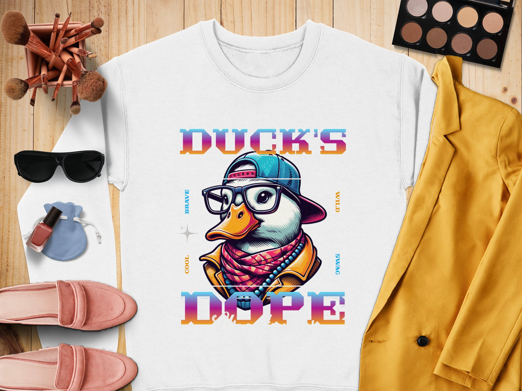 Garment Graphics offers a white t-shirt with a vibrant duck wearing glasses, a cap, and a scarf, accompanied by the bold text Ducks Dope. Style it effortlessly with sunglasses, makeup brushes, nail polish, pink shoes, and a yellow jacket for added flair.