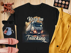 Garment Graphics graphic sweatshirt showcases a Keep on Trucking text and vibrant semi-truck design. Styled with makeup, brushes, sunglasses, pink shoes, a blue pouch, and a yellow jacket on a wooden surface for a relaxed vibe.