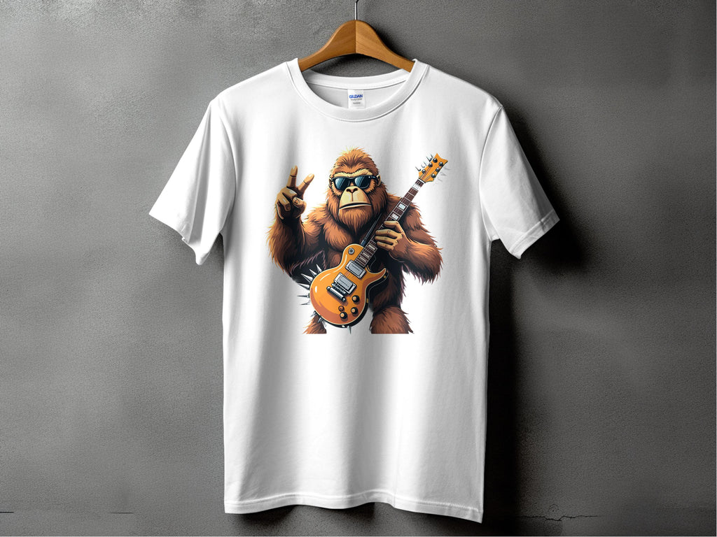A white T-shirt by Garment Graphics hangs on display, featuring a groovy gorilla in sunglasses playing an electric guitar and giving the peace sign. Ideal for music lovers, its set against a plain gray wall.