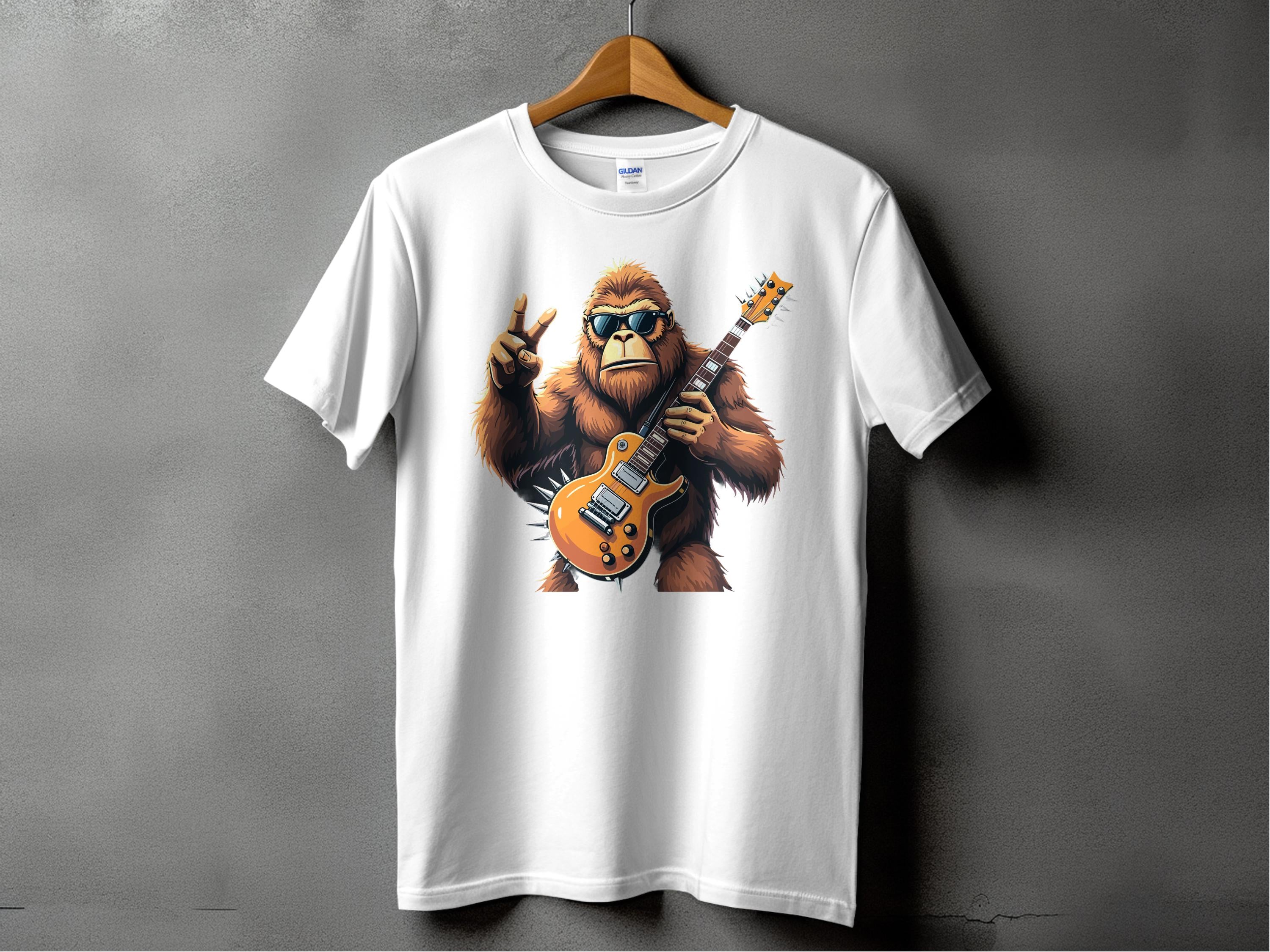 A white T-shirt by Garment Graphics hangs on display, featuring a groovy gorilla in sunglasses playing an electric guitar and giving the peace sign. Ideal for music lovers, its set against a plain gray wall.