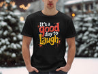 In a snowy outdoor scene, someone sports a vibrant Garment Graphics Its a Good Day to Laugh t-shirt, spreading cheer amid blurred snow-covered trees and warm lights.