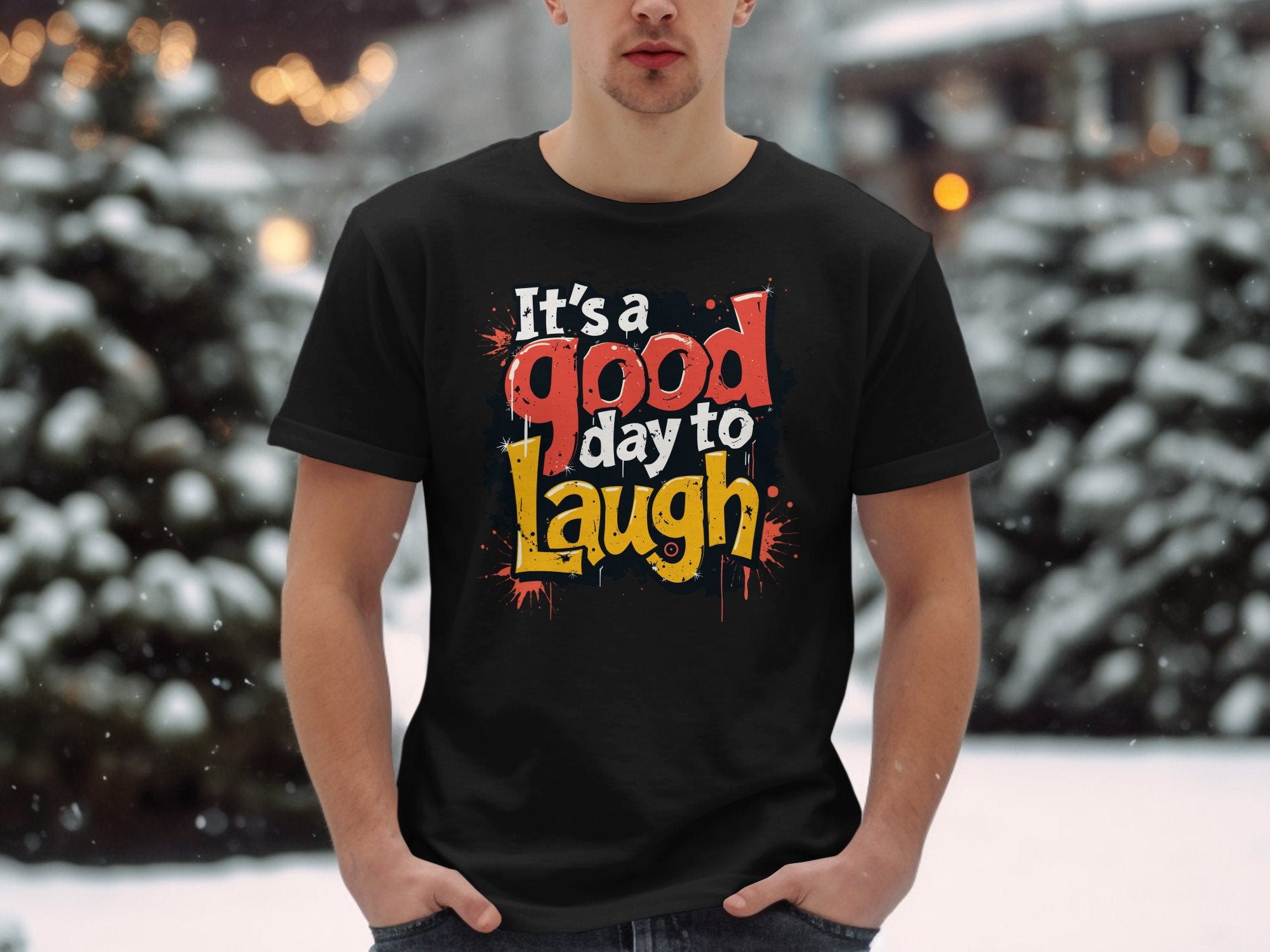 In a snowy outdoor scene, someone sports a vibrant Garment Graphics Its a Good Day to Laugh t-shirt, spreading cheer amid blurred snow-covered trees and warm lights.