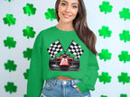 A woman in a vibrant green Garment Graphics sweatshirt featuring a racing car and checkered flags, perfect for motorsport fans, poses against a shamrock-covered wall. Her long brown hair cascades over denim shorts.