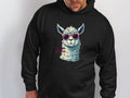 A person wears a Garment Graphics unisex black hoodie featuring an alpaca graphic wearing sunglasses. The phrase No Prob-Llama complements the illustration as they pose against a plain white background.