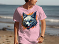 At the beach, someone flaunts a dynamic T-shirt from Garment Graphics with a colorful wolf design, embodying a fearless attitude against the waves and sand backdrop.