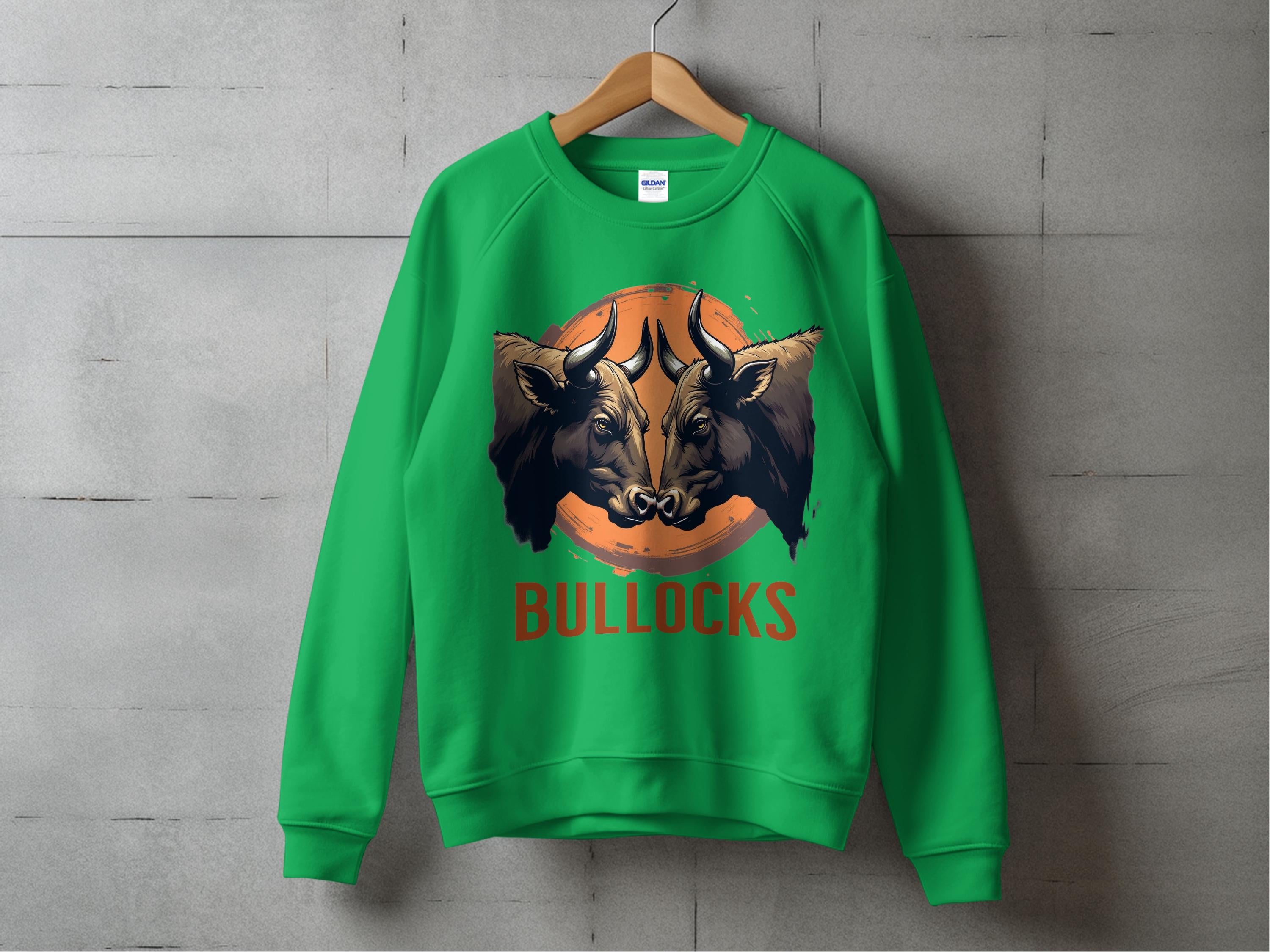 A green Garment Graphics sweatshirt with a bold bullock design hangs on a wooden hanger against a concrete wall. Unisex sizing lets everyone enjoy the bulls head illustration, with BULLOCKS in striking red letters below.