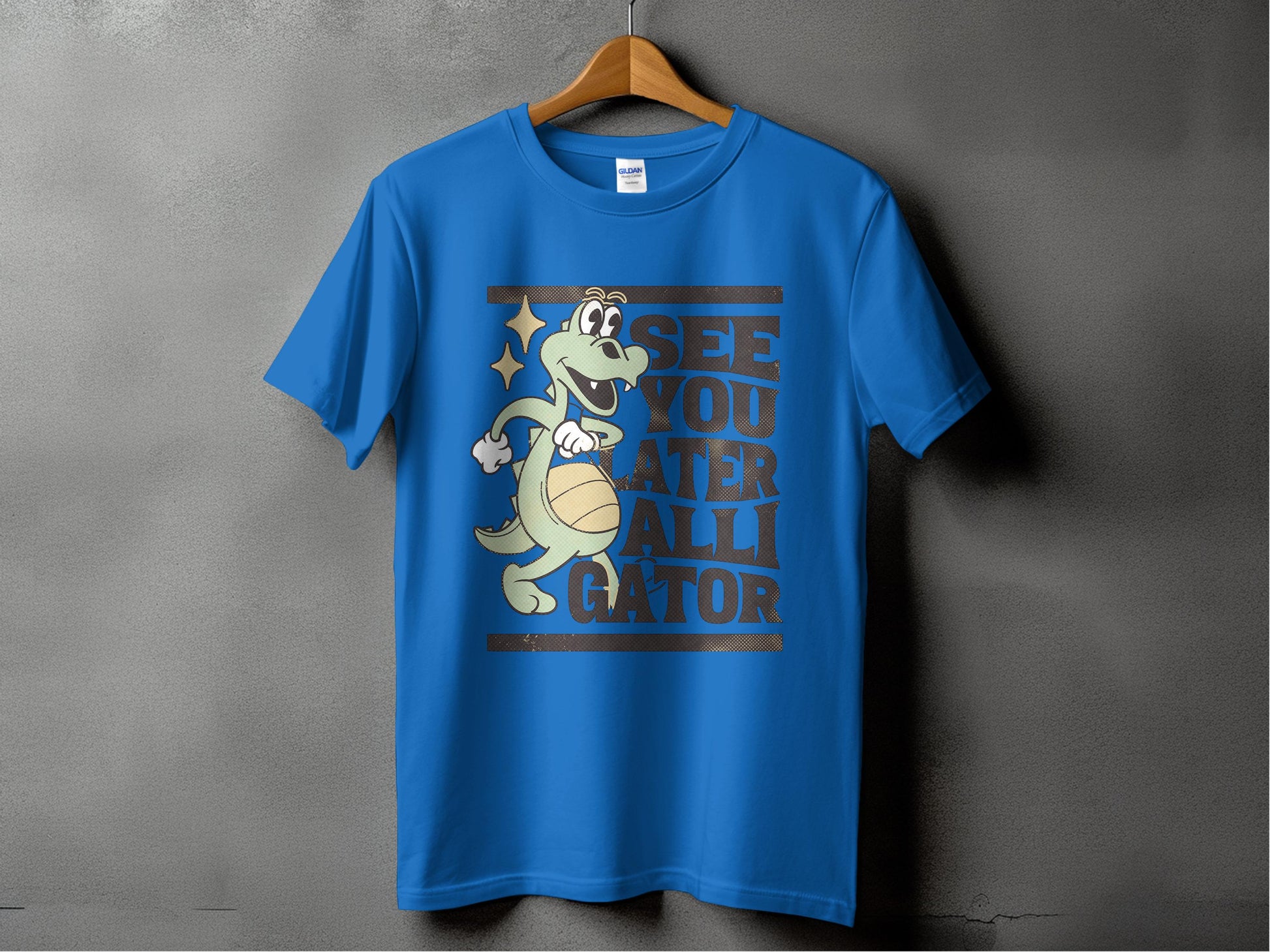 Against a gray backdrop, a Garment Graphics blue T-shirt displays a smiling cartoon alligator with a basketball and the phrase, See You Later Alligator, making it ideal for casual wear.