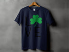 A Garment Graphics T-shirt, dark blue and hanging on a wooden hanger against a gray background, embodies Irish spirit. The word LOVE features a clover graphic as the O, making it ideal for a St. Patricks Day collection.