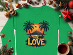 A Garment Graphics unisex green shirt, with a sunset between palm trees and One Love, sits on a wooden surface decorated with holiday ornaments, pinecones, baubles, and a steaming coffee.