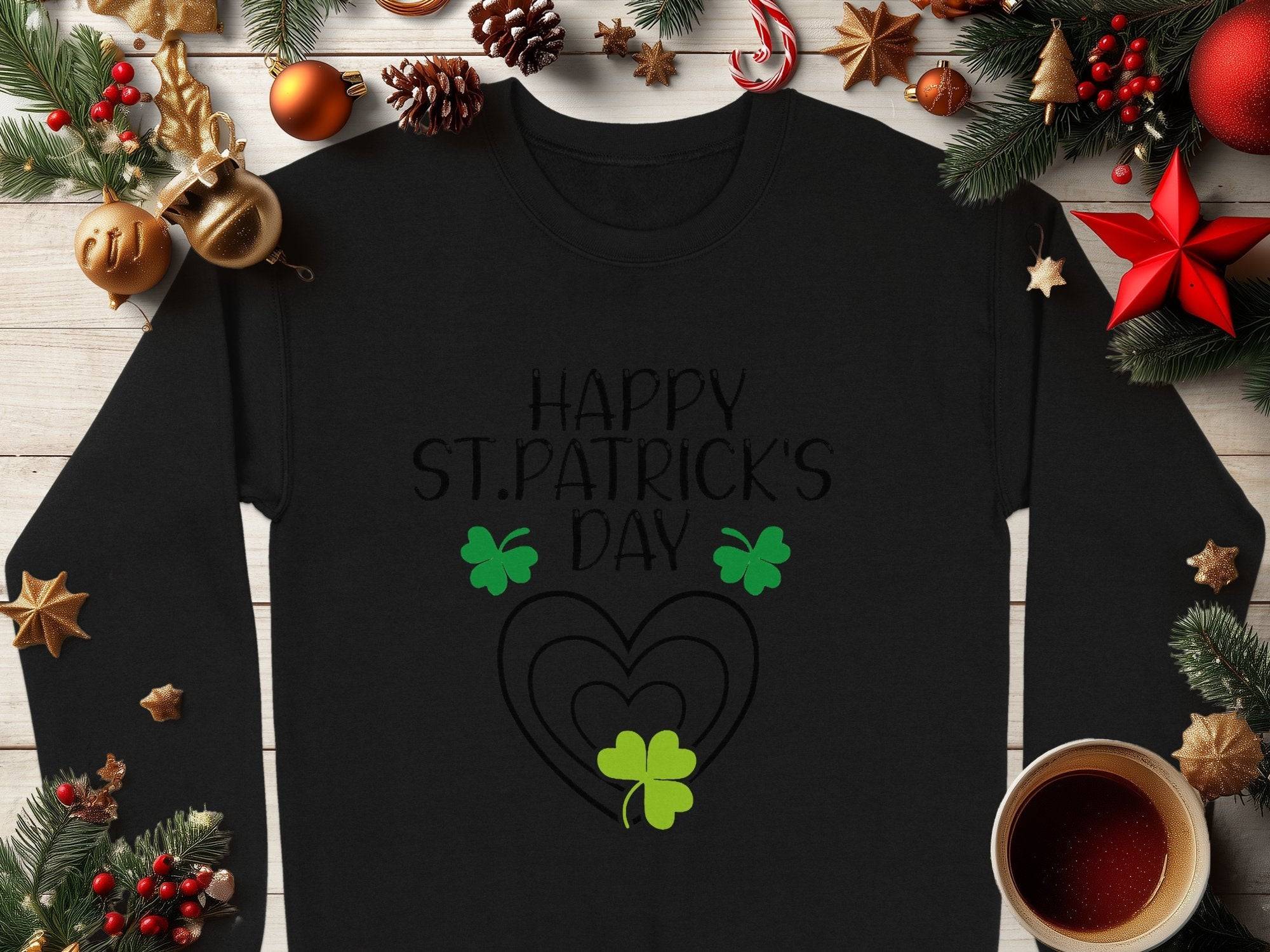 Garment Graphics offers a festive sweatshirt with black long sleeves, featuring Happy St. Patricks Day and a vibrant clover design of green shamrocks. It includes playful decorations like pine cones, baubles, cinnamon sticks, and a cozy coffee cup on a wooden background.