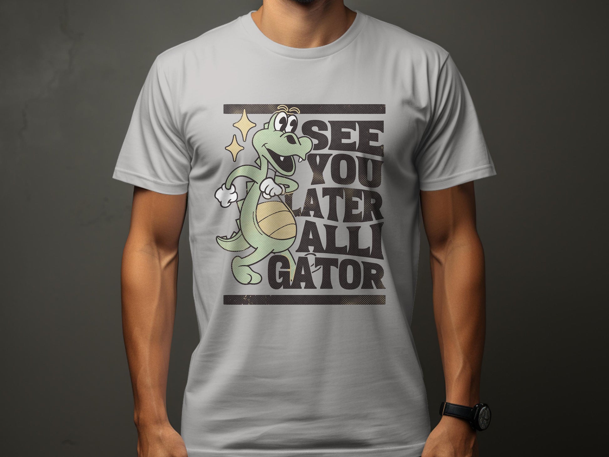 A person wears a Garment Graphics light gray t-shirt featuring a cartoon alligator with a basketball and star near its head. Ideal for casual wear, the shirt whimsically reads, See You Later Alligator.