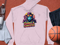 A light pink Garment Graphics hoodie features a vibrant blue gorilla with a hat and sunglasses, labeled Gorilla Gangster. Styled on a sports court with a basketball, black shorts, towel, and water bottle.