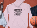 A Cleverly Disguised As A Responsible Adult hoodie by Garment Graphics in light pink, ideal for casual wear, with black text. It comes with a water bottle, white towel, black shorts, and an orange basketball displayed on a reddish-brown background.