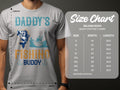 Someone wears a Garment Graphics gray T-shirt featuring Daddys Fishing Buddy with a fish and boat design. A size chart for Gildan 5000 heavy cotton T-shirts is on the right, offering sizes S to 5XL with width and length measurements in inches—ideal for fishing fans of all sizes.