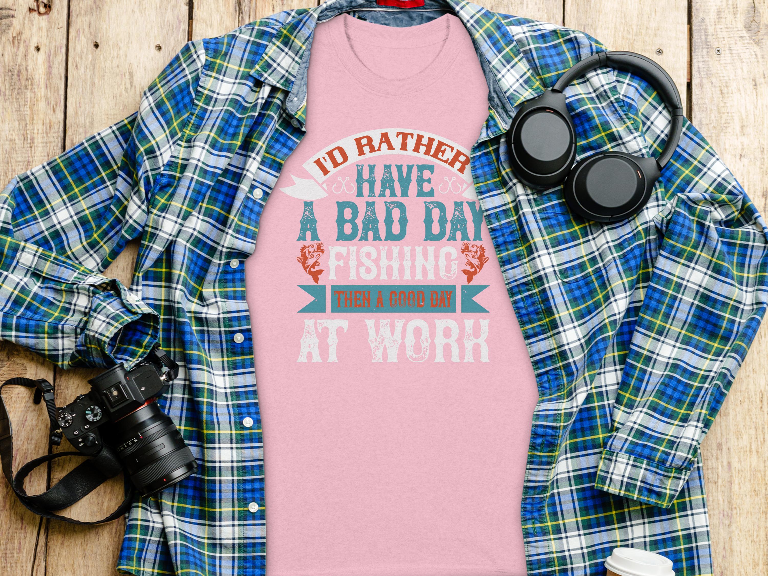 Garment Graphics plaid shirt over a fishing T-shirt with the text Id rather have a bad day fishing than a good day at work makes a great gift for anglers, styled next to a camera and headphones on wood.