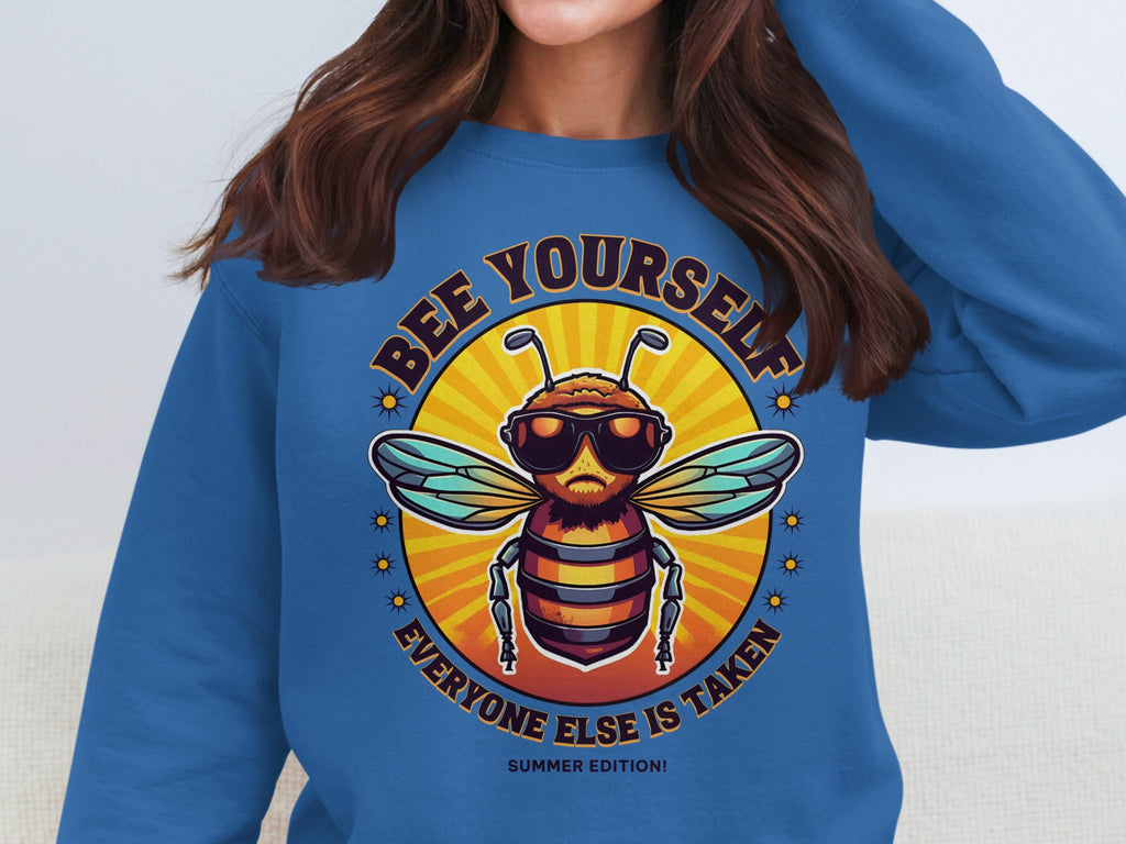 A person wears a quirky Garment Graphics Summer Edition sweatshirt featuring a bee with sunglasses and a beard. The vibrant text Bee Yourself is above, and Everyone Else Is Taken below. This fun, unisex piece is perfect for making a sunny statement.