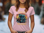 A woman wears a Garment Graphics light pink T-shirt featuring a truck graphic and the slogan KEEP ON TRUCKING, ideal for trucking fans. Blurred trees and snow in the background emphasize the winter setting.