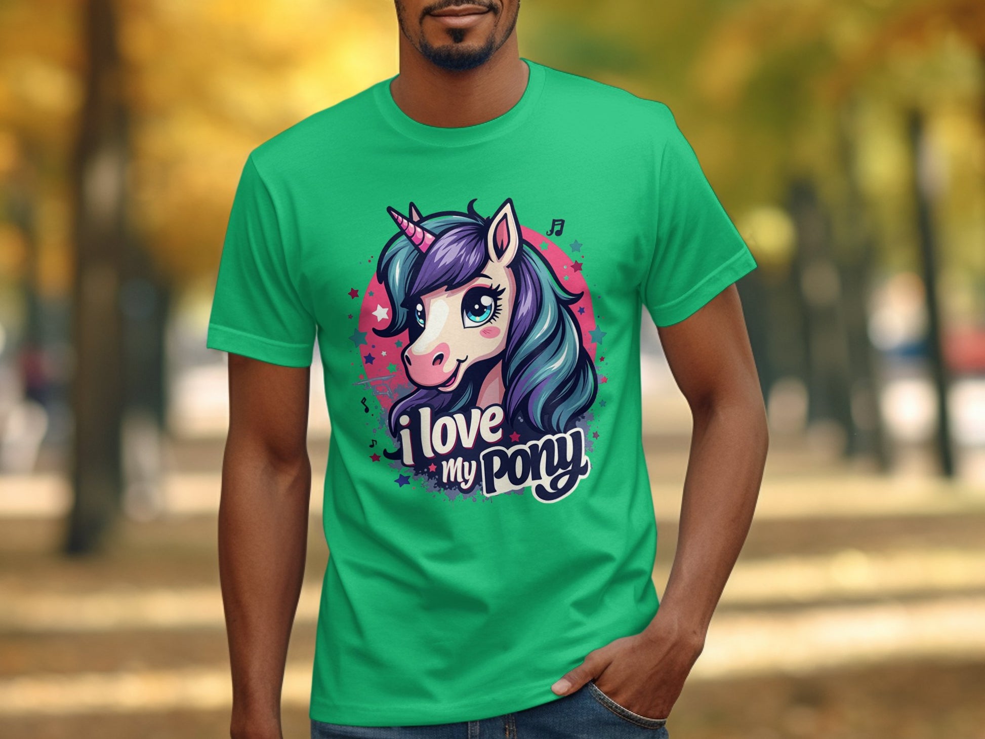 A unicorn enthusiast wears a green T-shirt from Garment Graphics, featuring a vibrant cartoon pony with a unicorn horn and the slogan I Love My Pony. In the background, a park is adorned with trees and scattered leaves.