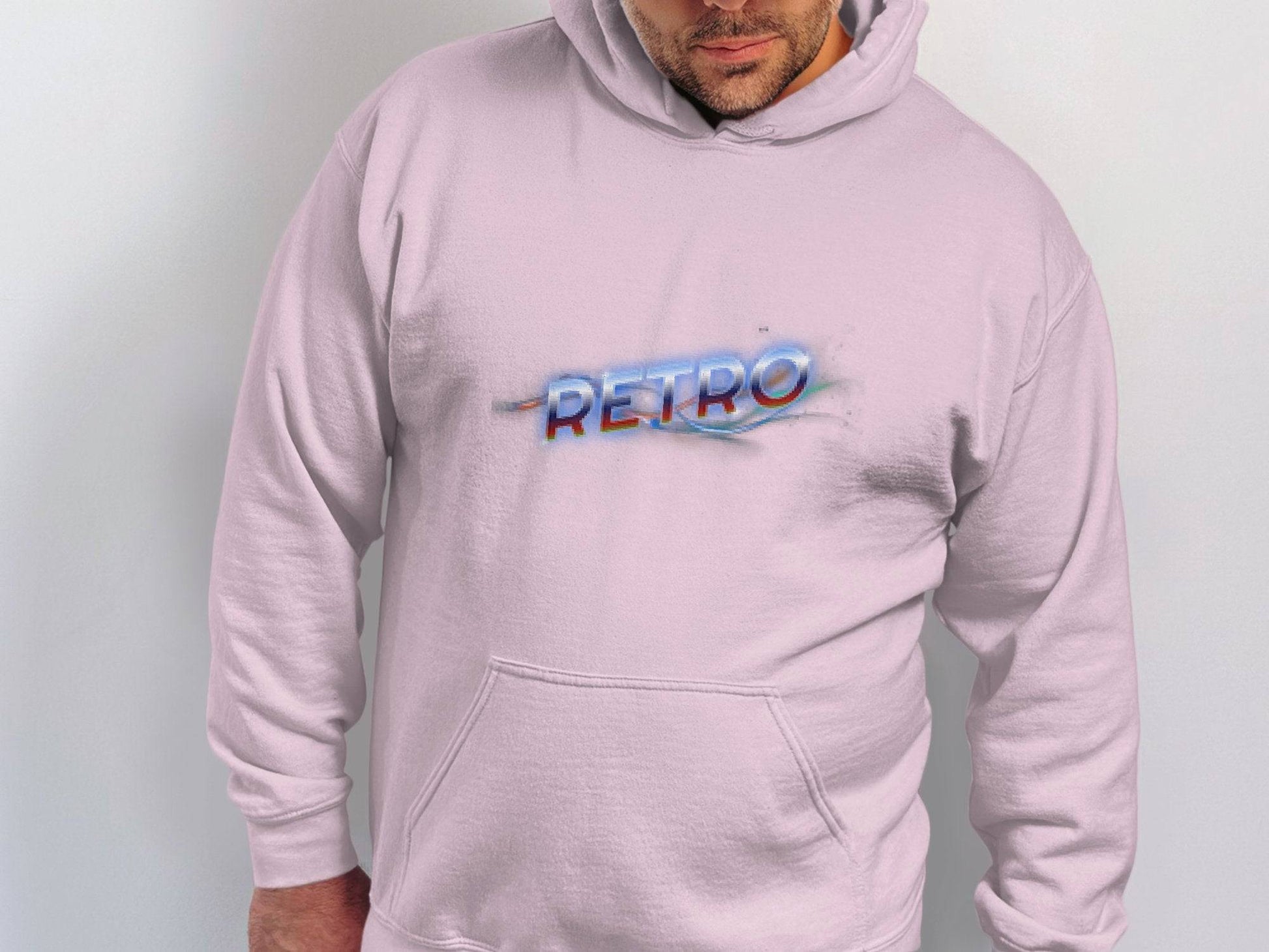 A person wears a Garment Graphics light pink hoodie with a front pocket, showcasing a vibrant Retro print in colorful, stylized font across the chest. This Retro 3D Graphic Hoodie offers a modern trendy look against its plain, light-colored background.