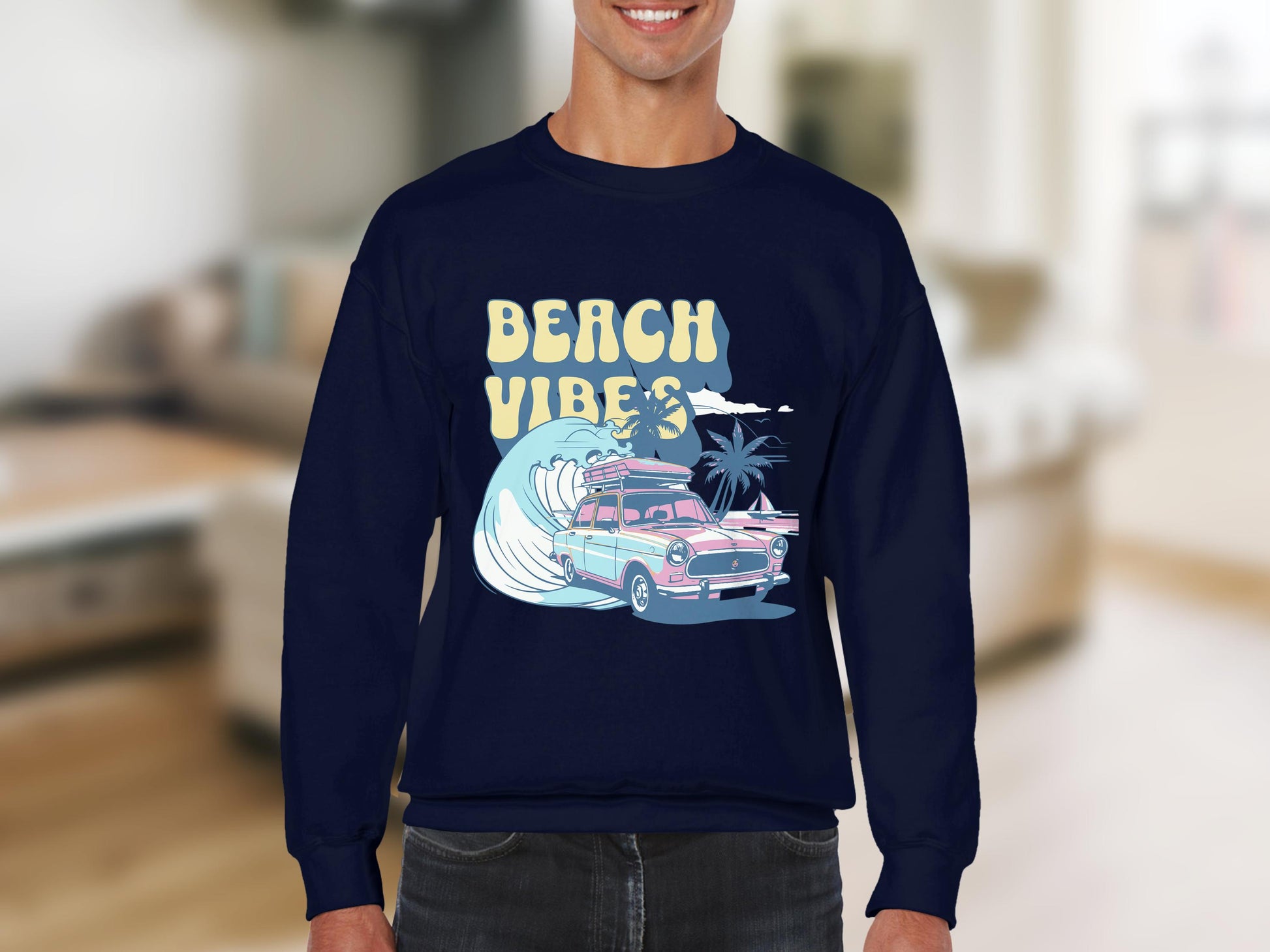 A person sports a Garment Graphics navy blue sweatshirt with a retro-themed graphic design, showcasing a classic car, wave, two palm trees, and flying seagull. The bold yellow BEACH VIBES lettering stands out against the blurred indoor background.