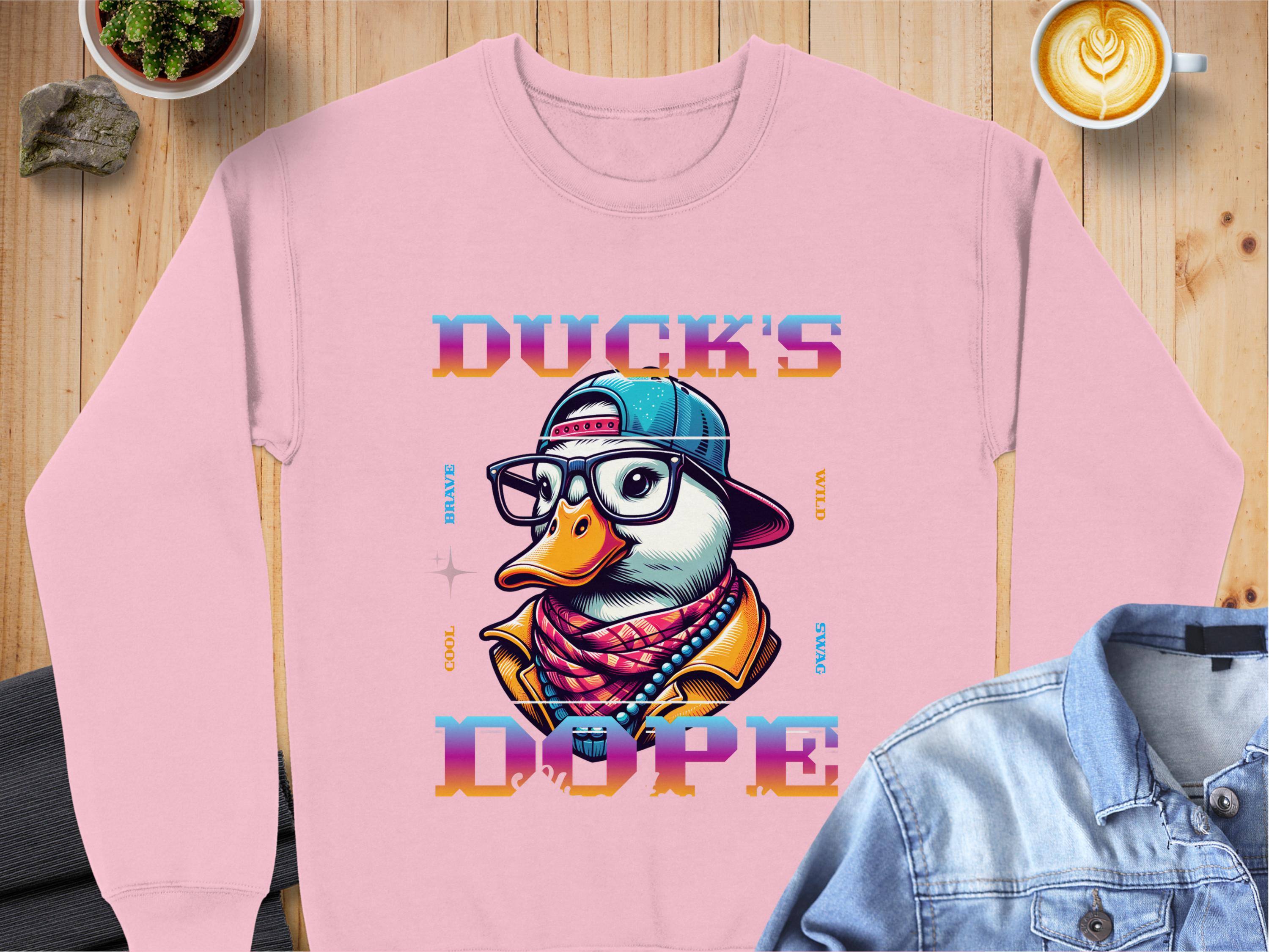 Garment Graphics offers a pink unisex sweatshirt with a cartoon duck in a cap, glasses, and scarf from the Brave Cool Swag collection. Made from medium-heavy fabric, it reads Ducks Dope and pairs stylishly with coffee, stones, and denim shirts for everyone’s comfort.