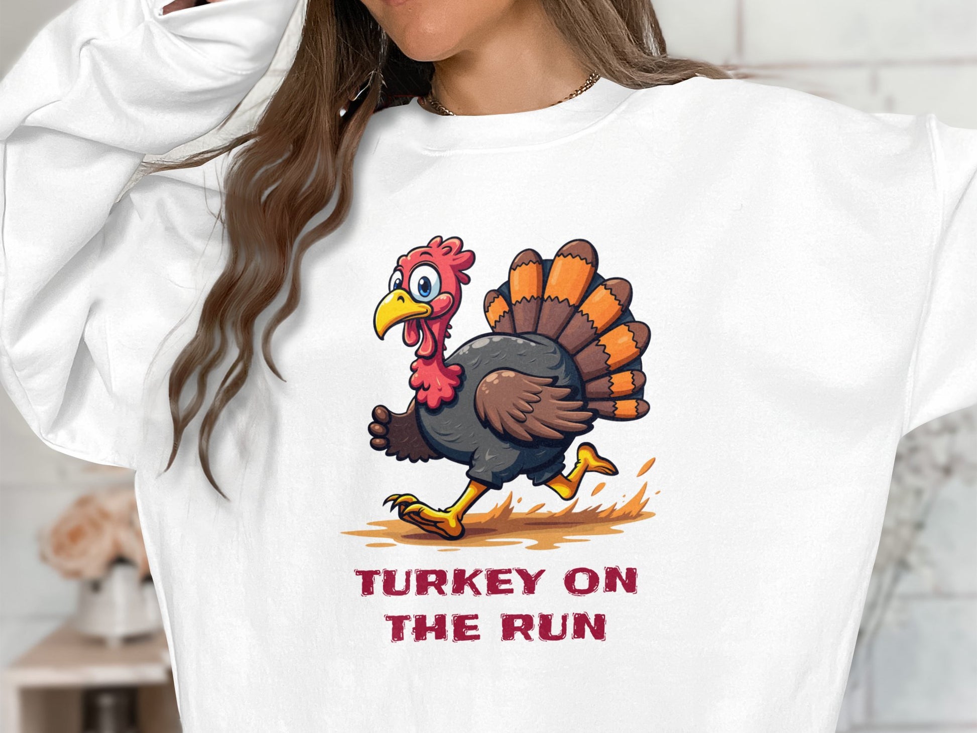 A person is wearing a Garment Graphics white sweatshirt with a humorous cartoon turkey design featuring red and orange feathers, a surprised expression, and the text TURKEY ON THE RUN. This funny graphic sweatshirt offers unisex sizing.