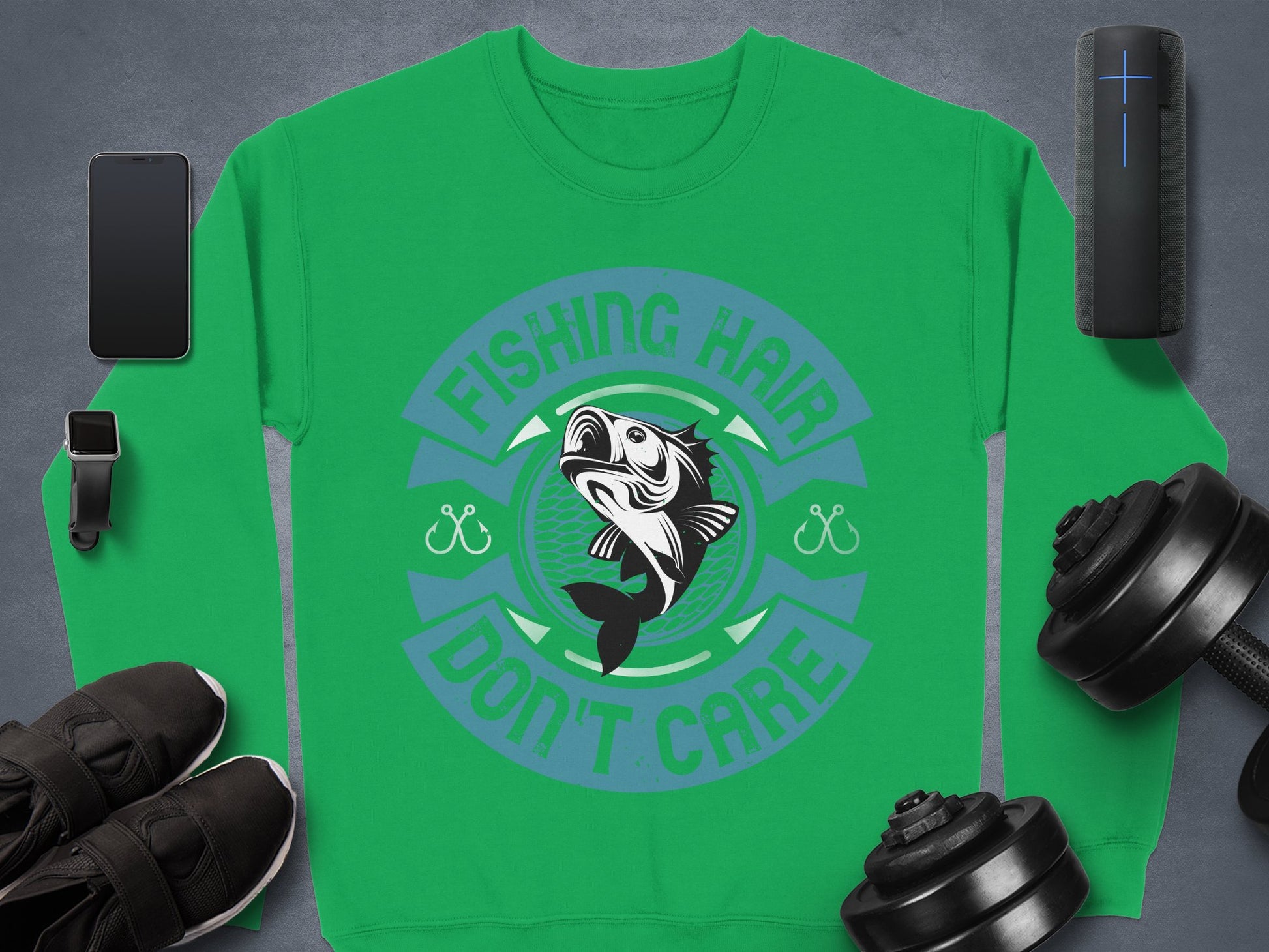 Garment Graphics fishing sweatshirt showcases a vibrant fish graphic with the quirky text Fishing Hair Dont Care. Its accompanied by a smartphone, smartwatch, shoes, Bluetooth speaker, and dumbbells on a gray background—perfect for any fishing enthusiasts collection.