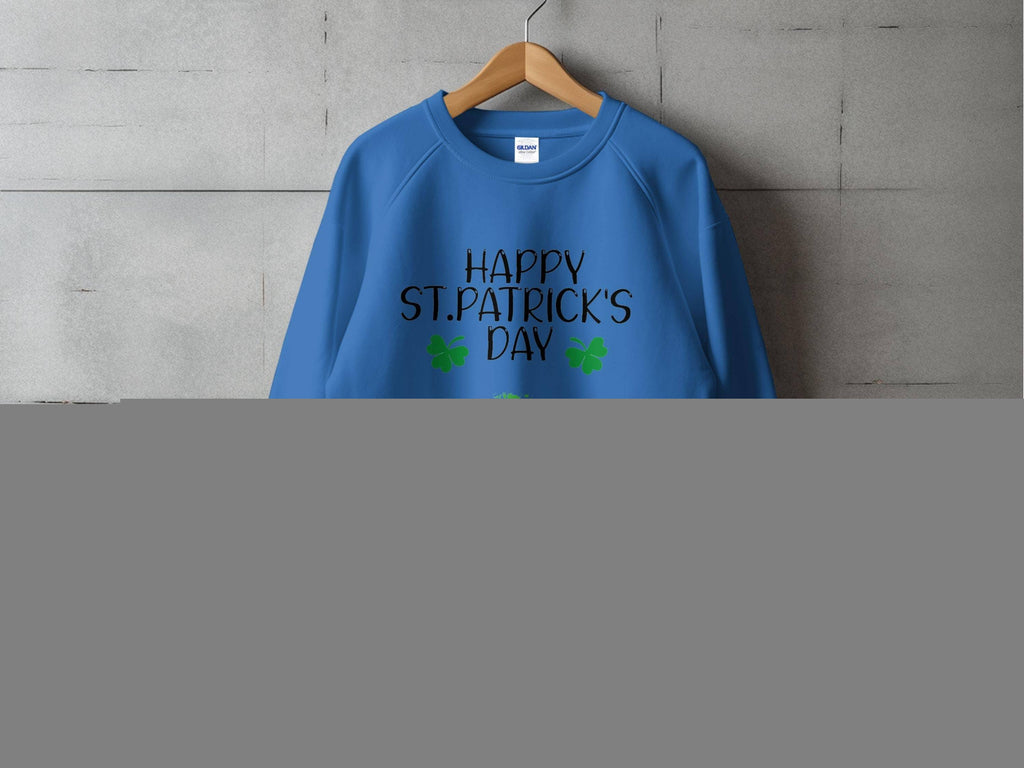 Displayed on a wooden hanger against a gray wall, the blue sweatshirt by Garment Graphics features Happy St. Patricks Day in bold black text, complemented by two green shamrocks and a playful clover kiss below, perfectly capturing the festive spirit.