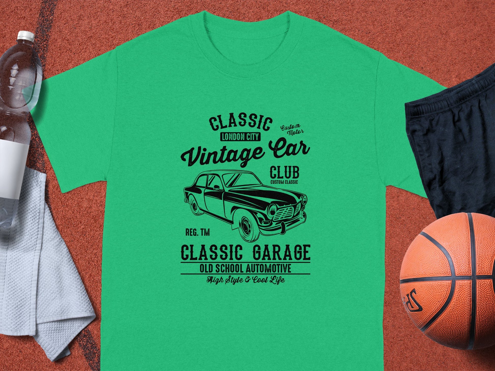 A Garment Graphics green t-shirt with Classic London City Vintage Car Club. Custom Culture. Classic Garage. Old School Automotive is displayed with a basketball, water bottle, striped towel, and black shorts on a sports court, ideal for vintage car fans.