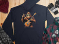 The Garment Graphics gorilla hoodie, showcasing a gorilla holding an electric guitar and making a peace sign, pairs perfectly with a red knit beanie, striped gloves, plaid shirt, and green flannel on a wooden surface—ideal for music lovers.