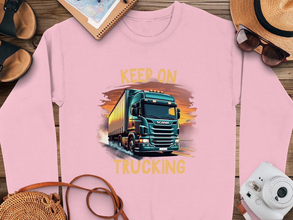 Garment Graphics offers a pink graphic sweatshirt for truck enthusiasts featuring a truck illustration with Keep On Trucking above and below. Its artistically presented on wood with accessories like a camera, sunglasses, hat, notebook, and sandals.